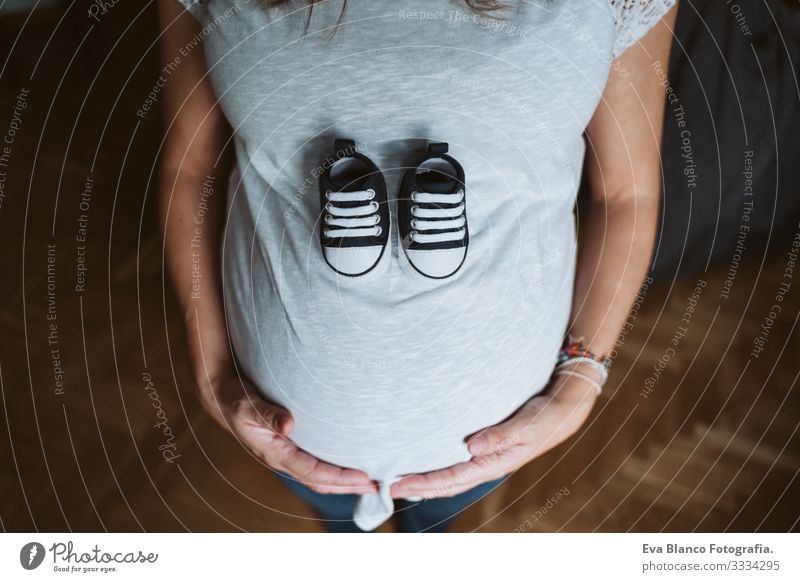 junge schwangere Frau zu Hause, die Babyschuhe hält heimwärts Bett Schwangerschaft erwartend bauchfrei Tag liegen Zärtlichkeit Vergnügen Innenarchitektur