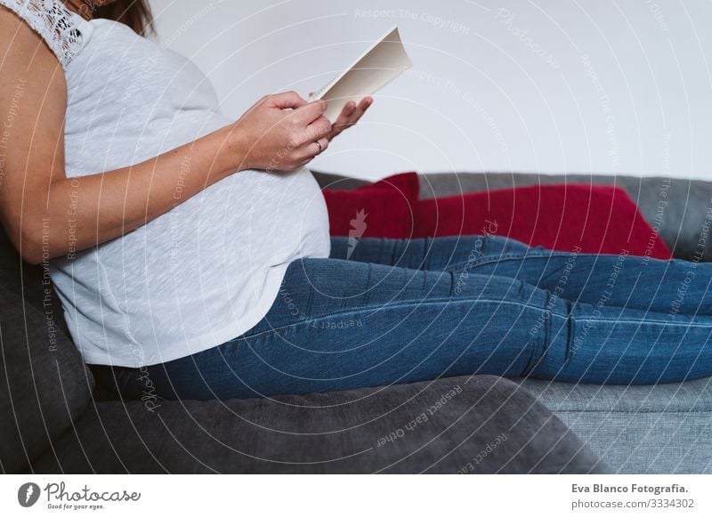 junge schwangere Frau zu Hause, die ein Buch liest Jugendliche Schwangerschaft lesen heimwärts Mutterschaft Leben Lounge bauchfrei Erholung Mitte heiter