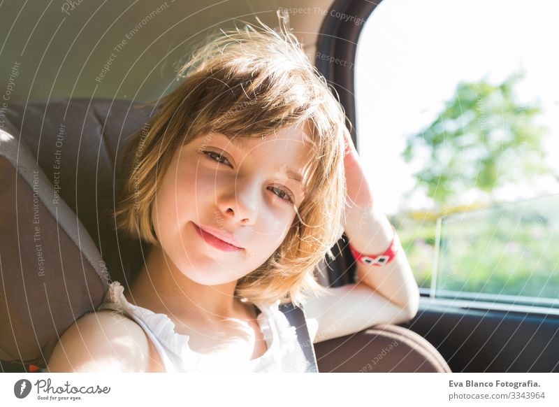 süßes Kleinkind, blondes Mädchen, im Autositz angeschnallt, glücklich wird sich auf den Weg der Straße machen, Sonnenblendung reflektiert Gürtel Sommer klein