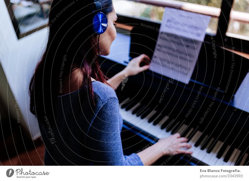 junge Frau, die beim Klavierspielen ein Notenblatt in der Hand hält. Musikkonzept im Innenbereich. Rückansicht Stil Mensch Schlüssel Hinweis Schulunterricht