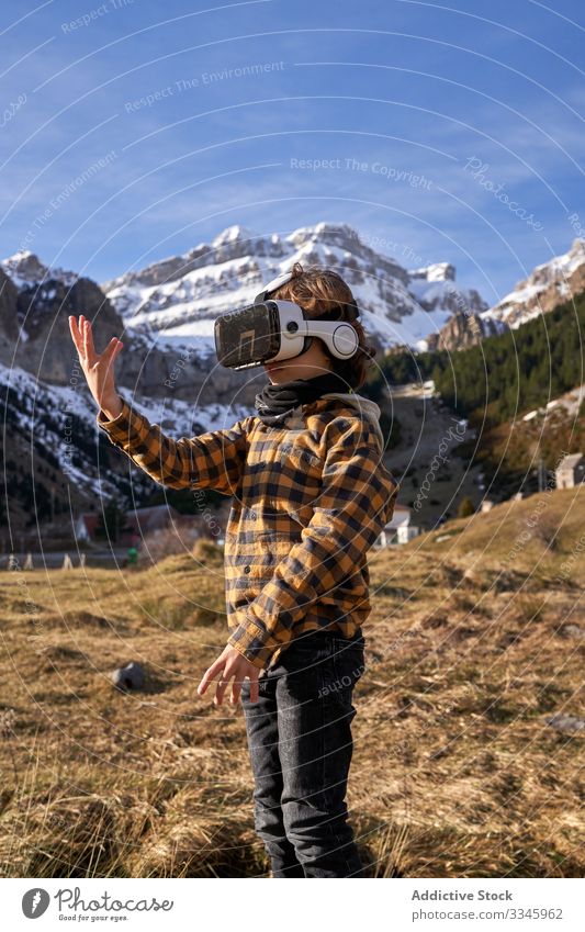 Auf Stein stehender Junge mit VR-Brille gegen Berg Natur Tal Berge u. Gebirge virtuell Realität Headset modern Gerät Entertainment erkunden Gelände