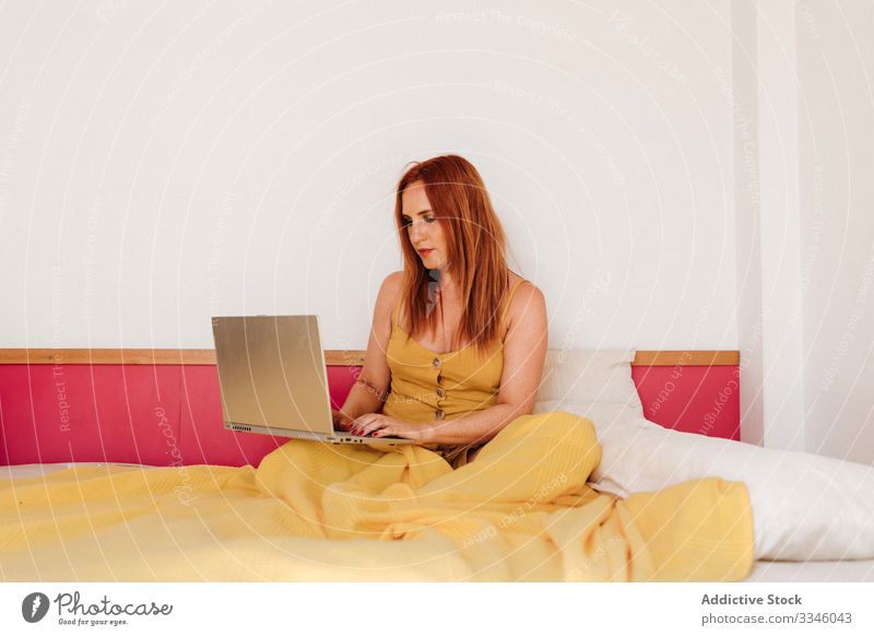 Frau, die zu Hause am Laptop im Bett arbeitet heimwärts benutzend Browsen freiberuflich Lügen Morgen beschäftigt klug gelb Kleid Lifestyle jung Internet Sitzen