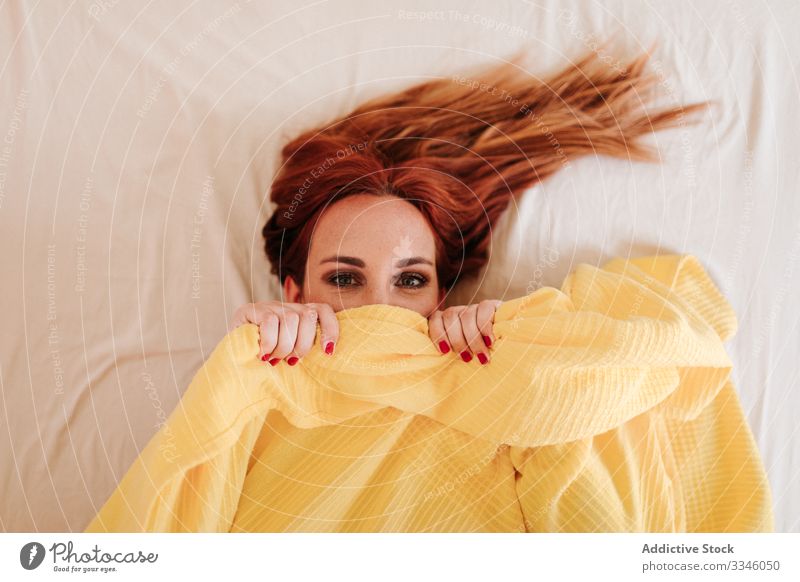 Positive Dame versteckt sich zu Hause unter einer Decke Frau Lügen Bett versteckend Morgen Sitzen Deckung gelb Spaß unten sich[Akk] entspannen ruhen Lächeln
