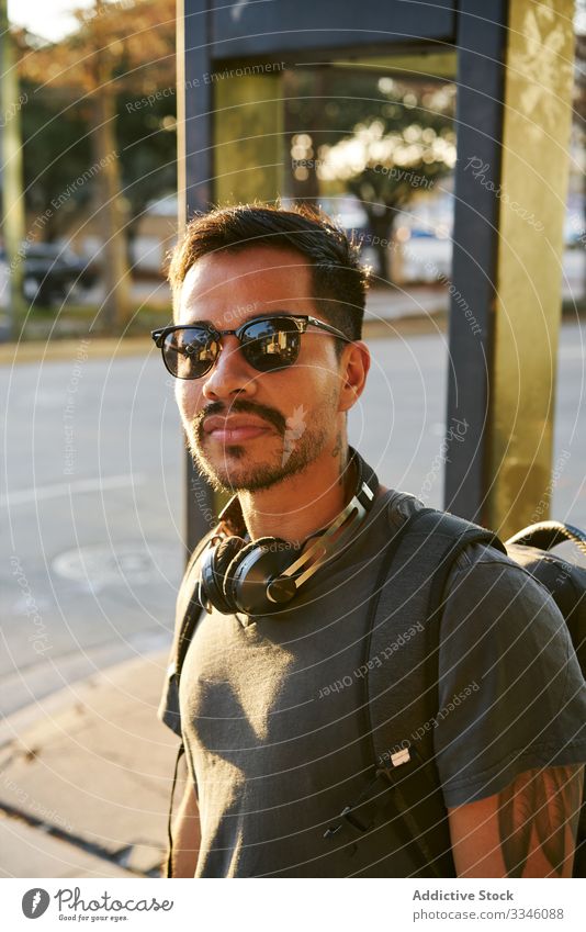 Zeitgenössischer Hispanoamerikaner auf der Straße in der Stadt Mann laufen Großstadt Sonnenuntergang Sonnenbrille lässig Kopfhörer Zubehör Rucksack Hipster