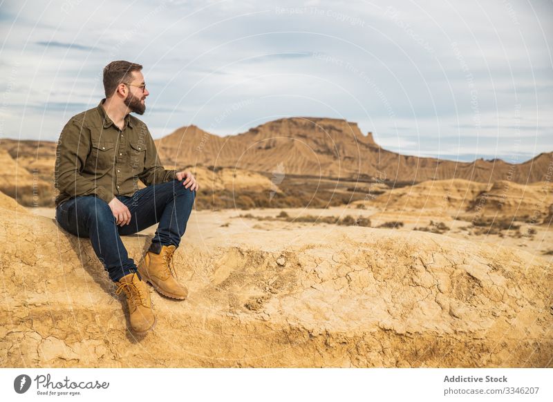 Junger Mann sitzt im Urlaub in der Nähe einer Klippe in der Wüste Tourismus Berge u. Gebirge wüst Felsen Stein lässig Sitzen Sonnenbrille stylisch Blauer Himmel