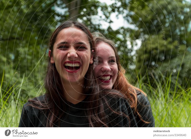 Zwei Freundinnen verschiedener Rassen lachen im Freien Freude schön Frau Erwachsene Freundschaft Jugendliche Natur Gras Park Umarmen Fröhlichkeit Zusammensein