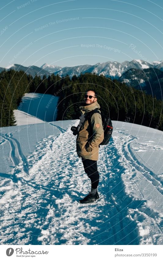 Ein Mann im Schnee auf einem Berg an einem sonnigen Tag mit Aussicht auf die Alpen. Wandern im Winter. Mensch Winterwanderung maskulin Junger Mann Jugendliche