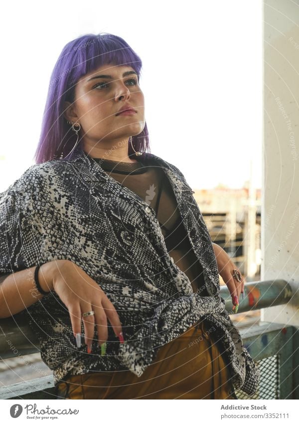 Frau mit lilafarbenen Haaren lehnt auf Metallzaun und schaut weg stylisch urban purpur Frisur Konstruktion glänzend Struktur Revier selbstbewusst Mode jung Stil