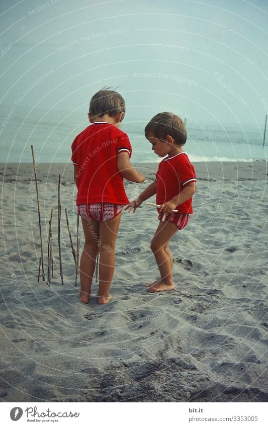 Zwei kleine Mädchen im Partnerlook, spielen am Strand, bauen mit Stöcken einen Zaun und lauschen dem Meer zu. Kindererziehung Freiheit Spielen Glück Natur