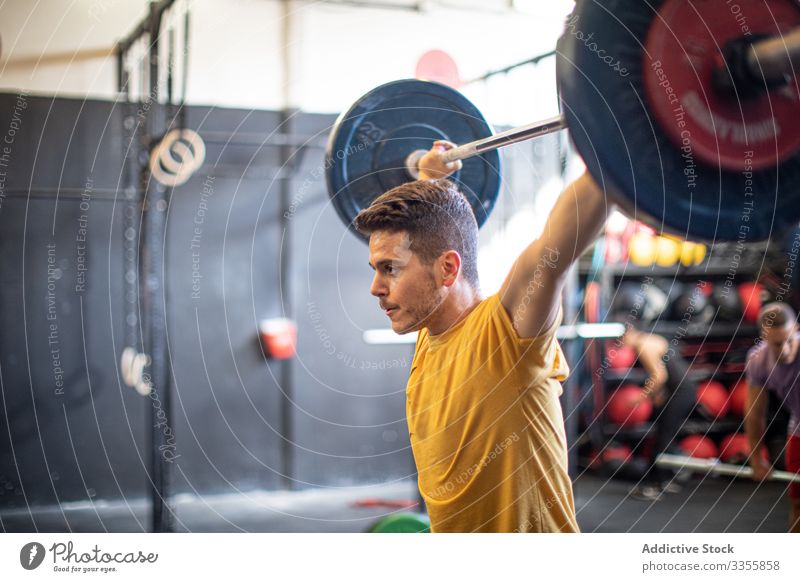 Muskulöser Mann hebt Langhantel im modernen Fitnessstudio Sportler Training Gewichtheben Curl-Hantel schwer anstrengen Erwachsener stark männlich angespannt