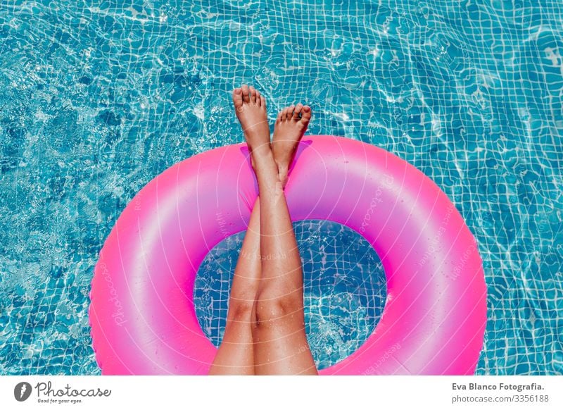 nicht wiedererkennbare Teenagerin, die auf rosa Donuts in einem Pool schwimmt. Sonnenbrille tragen und lächeln. Spaß und sommerlicher Lebensstil Aktion