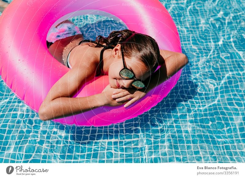 Ein wunderschöner Teenager schwimmt auf rosa Donuts in einem Pool. Sonnenbrille tragen und lächeln. Spaß und sommerlicher Lebensstil Aktion Schwimmbad