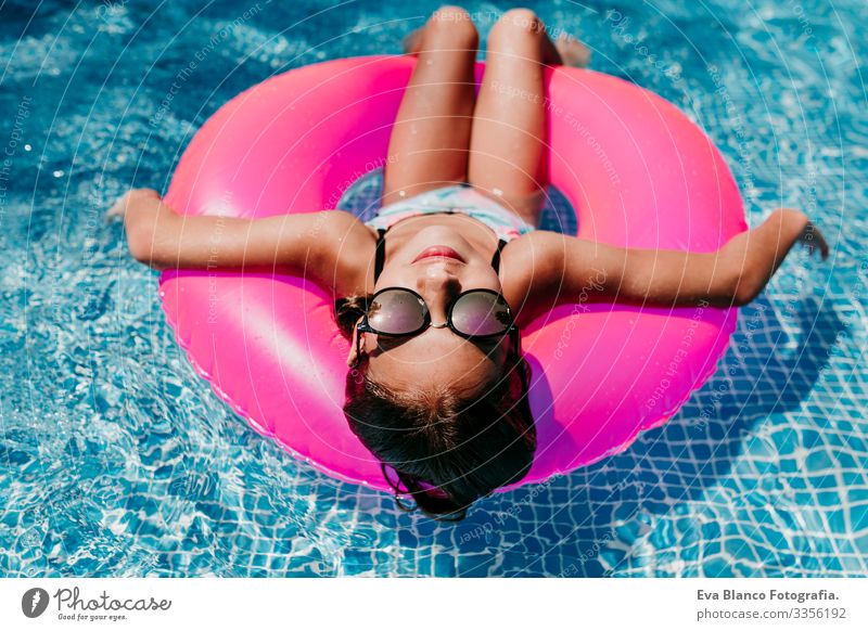 Ein wunderschöner Teenager schwimmt auf rosa Donuts in einem Pool. Sonnenbrille tragen und lächeln. Spaß und sommerlicher Lebensstil Aktion Schwimmbad