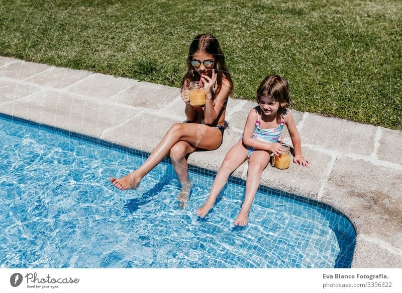 zwei schöne Schwestern am Pool, die Orangensaft trinken, Sommerzeit Kind Familie & Verwandtschaft zwei Schwestern Freundschaft Zusammensein genießen fliegend