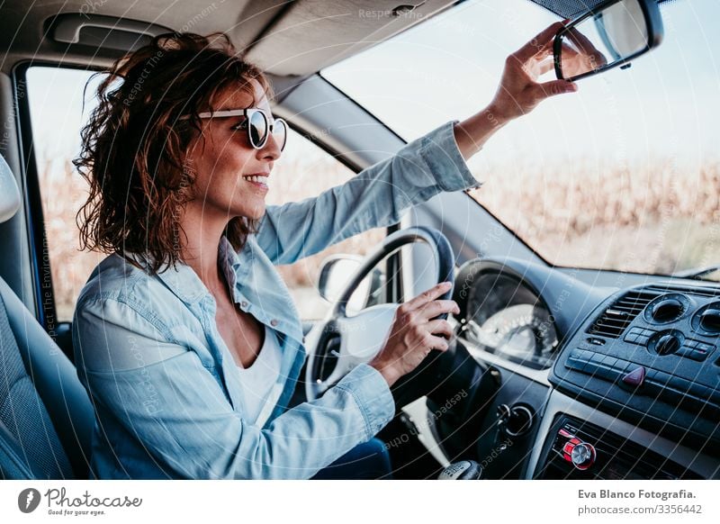 junge schöne Frau, die ein Auto fährt und den Rückspiegel verstellt. reisekonzept Jugendliche fahren PKW Sonnenstrahlen Sonnenbrille Ferien & Urlaub & Reisen