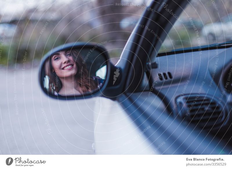 Junge Frau, die in der Stadt Auto fährt. Porträt einer schönen Frau in einem Auto, die aus dem Fenster schaut und lächelt. Spiegelung im Rückspiegel. Reise- und Urlaubskonzepte
