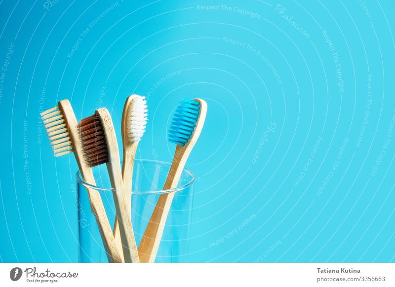 Zahnbürsten aus Holz mit einem Glasbecher auf blauem Hintergrund. Lifestyle Behandlung Wellness Leben Bad Umwelt Natur Verpackung Kunststoff frei frisch modern