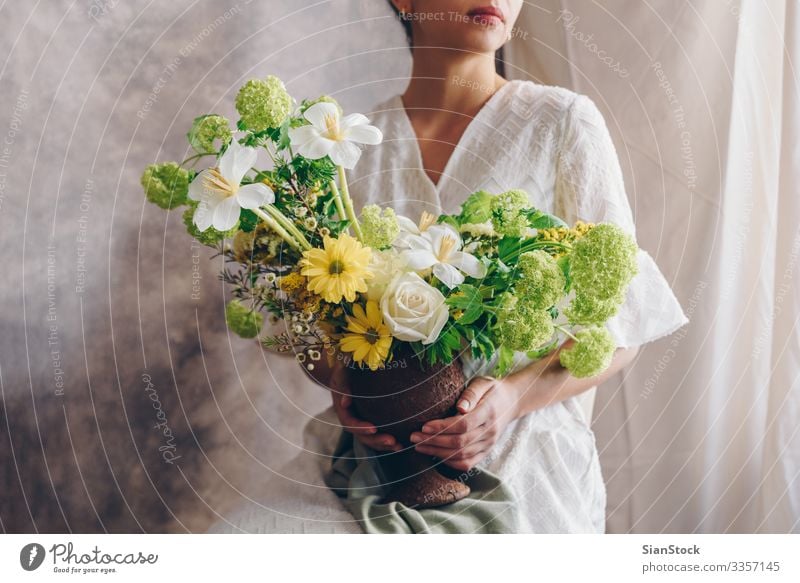 Junge Frau in einem weißen Kleid, die eine Vase mit Blumen hält. Lifestyle elegant Stil Glück schön Stuhl Hochzeit Erwachsene Lippen Hand brünett Blumenstrauß