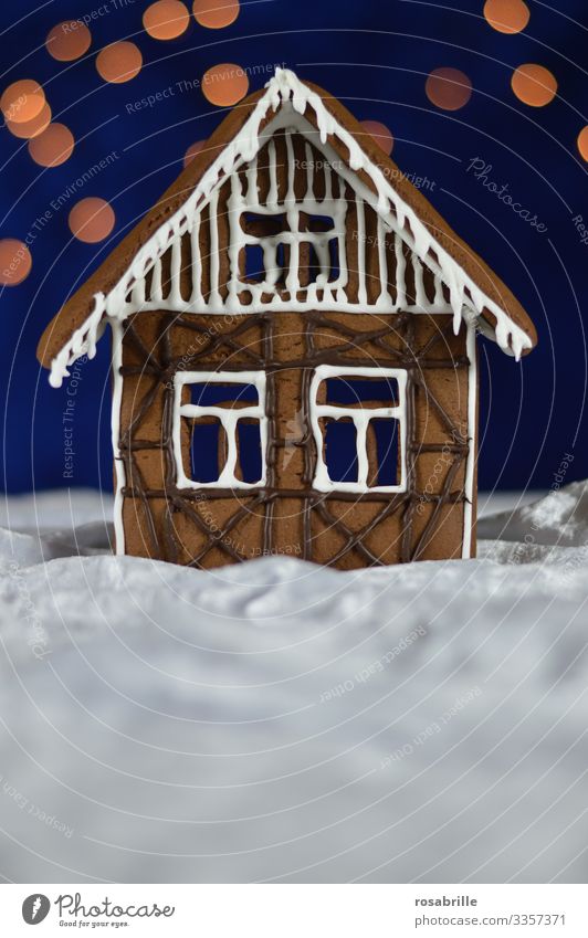 Lebkuchenhaus Fassade mit Zuckerguß und Schokoladenverzierung als Fachwerk auf weissem Samt, der wie Schnee aussieht, vor dunkelblauem Hintergrund mit Bokeh-Punkten als Sterne
