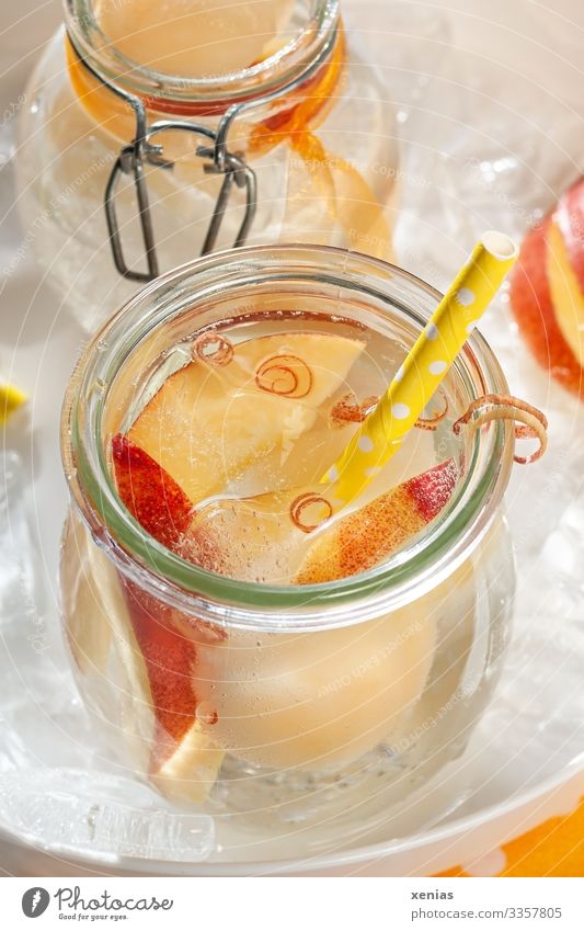 Kühle Limonade mit saftiger Nektarine in Glas und gelbem Trinkhalm auf weißem Tablett voller Eiswürfel Erfrischungsgetränk Frucht Getränk Vitamin Pfirsich