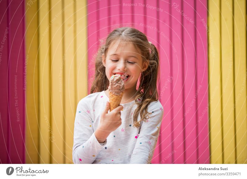 Süßes kleines Mädchen isst Schokoladeneis. Lächelnd und lachend. Bunte rosa und gelbe Wand im Hintergrund. Leuchtendes Sommerkonzept schön hell Café offen