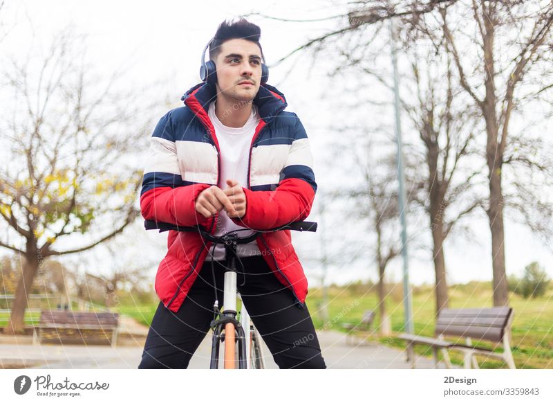 Hübscher, hipper junger Mann, der eine Fahrradtour genießt und ein Smartphone benutzt, während er über Kopfhörer Musik hört Straße Menschen männlich Person