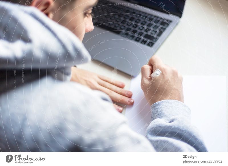 Rückenansicht eines jungen Mannes, der zu Hause neben dem Laptop auf Papier schreibt Tisch Schule lernen Studium Arbeit & Erwerbstätigkeit Beruf Büroarbeit