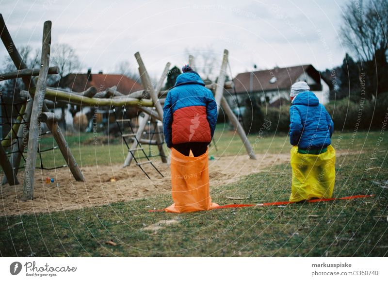 Zwei Sackhüpfen der Jungen analoge Fotografie 35mm Filmfotografie Filmscan Scan Leica R7 farbenfroh rot gelb im Freien Kind Kinder Kindheit Spielplatz