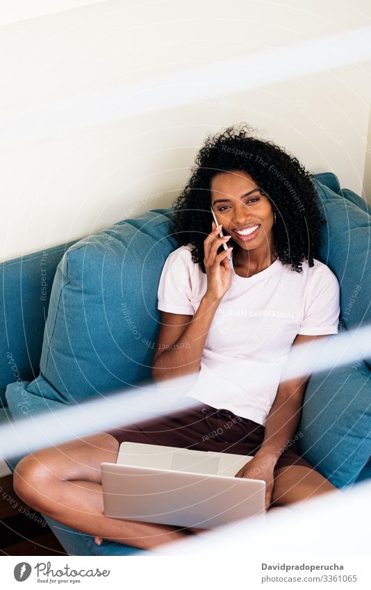 Inhalt Afroamerikanerin nutzt Geräte zu Hause Frau Laptop Armsessel freiberuflich Telefonanruf Smartphone benutzend Browsen gemütlich Komfort Talkrunde reden