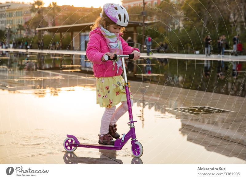 Süßes Kind mit Helm auf einem Roller auf dem Stadtplatz. Aktion offen Kindheit Großstadt niedlich Frankreich Freude Mädchen Glück Schutzhelm Freizeit & Hobby