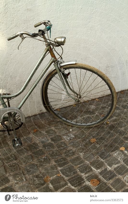 alt l altes, nostalgisches Rad im Retro-Stil, steht geparkt vor weisser, heller Hauswand auf Kopfsteinpflaster. Vorderteil, Lenker, Lampe, Licht, Reifen, Bremse von grauem Rad parkt in der Stadt. Diebstahlgefahr von altem Fahrrad, nicht abgeschlossen.