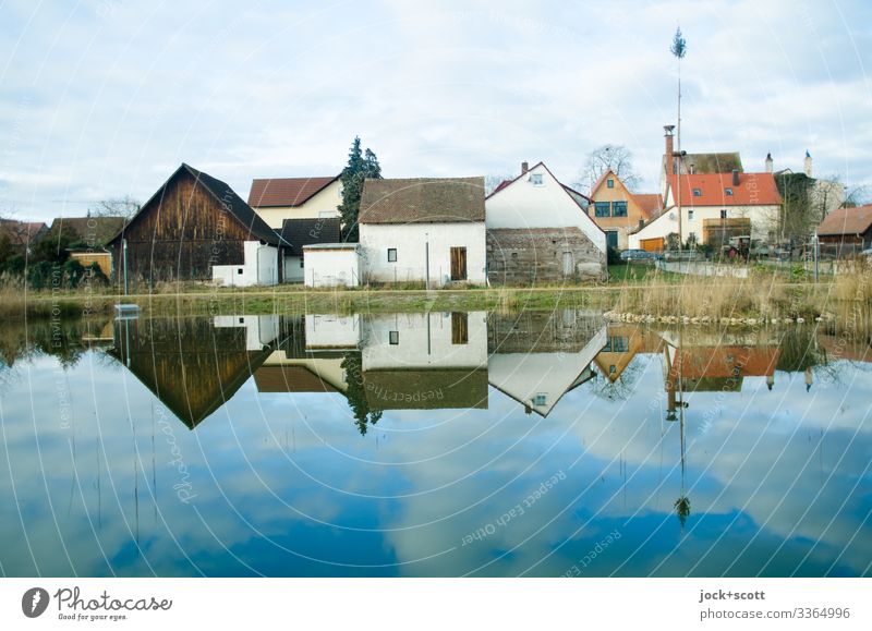 Ländliche fränkische Häuser an einem idyllischen Teich gelegen die sich in ihm spiegeln Franken Karpfenteich ländlich Himmel Wolken Winter
