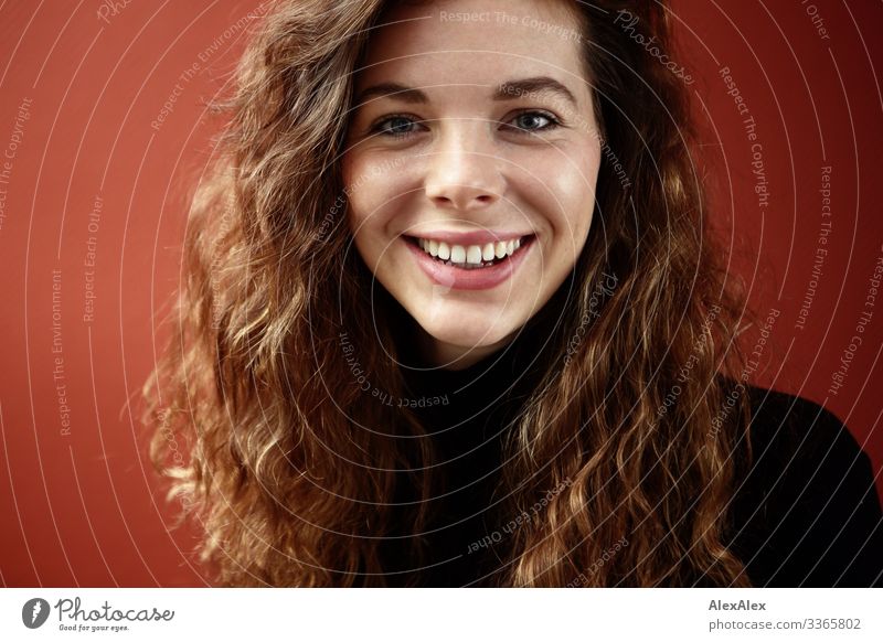 Portrait einer lächelnden, jungen Frau mit Grübchen vor einer roten Wand Häusliches Leben Junge Frau Jugendliche Gesicht 18-30 Jahre Erwachsene Pullover brünett