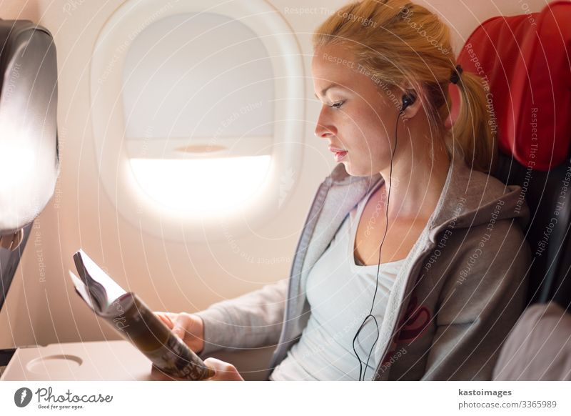 Frau, die eine Zeitschrift liest und im Flugzeug Musik hört. Lifestyle Erholung lesen Ferien & Urlaub & Reisen Ausflug Entertainment Wirtschaft Business Mensch