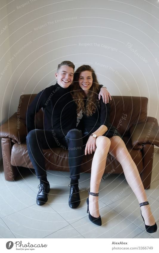 Junger Mann und junge Frau sitzen auf einer braunen Leder- Couch innig zusammen und lächeln Lifestyle Stil Freude schön harmonisch Häusliches Leben Sofa Raum