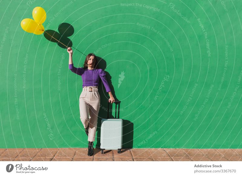 Junge Frau mit Luftballons und Koffer steht neben grüner Wand reisen Feiertag Urlaub Glück sorgenfrei jung Gepäck Tourismus Reise Tasche stylisch modisch modern