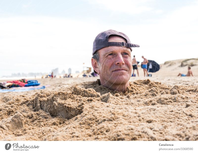 Mann mit Kappe steckt Kopf aus dem Sand am Strand Farbfoto Außenaufnahme Portrait Kappe," Blau weißer Hintergrund Himmel Sommer Meer Urlaub Menschen eingraben