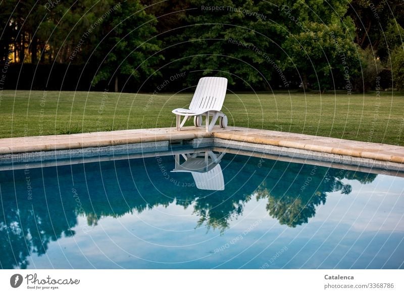 Corona thoughts | Daheim bleiben-      Einsamer Liegestuhl steht am Schwimmbeckenrand, der Himmel spiegelt sich im Wasser, ein gepflegter Rasen und eine Baumreihe sind im Hintergrund zu sehen, die Sonne geht unter.