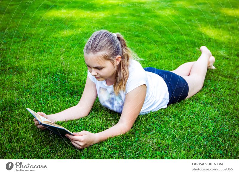 Teenager-Mädchen liegt auf grünem Gras und liest im Park ein Buch Lifestyle Glück schön Gesicht Freizeit & Hobby lesen Sommer Garten Schule lernen Mensch Frau