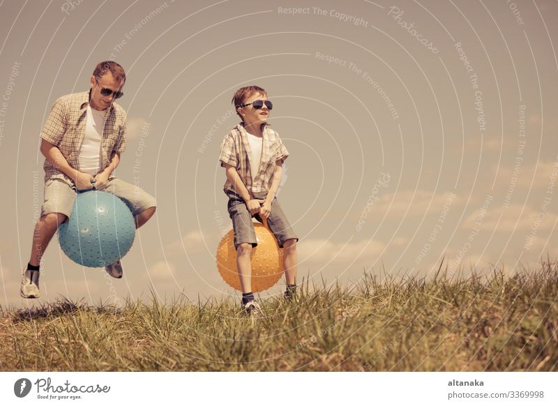 Vater und Sohn spielen zur Tageszeit auf dem Spielfeld. Die Menschen haben Spaß im Freien. Sie springen auf aufblasbaren Bällen auf dem Rasen. Konzept der freundlichen Familie.