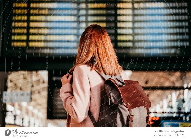 junge Frau am Bahnhof, die auf die Zieltafel schaut. Konzept für Reisen und öffentliche Verkehrsmittel Bildschirm Ausflugsziel reisen Rucksack Rückansicht