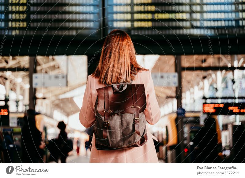 junge Frau am Bahnhof, die auf die Zieltafel schaut. Konzept für Reisen und öffentliche Verkehrsmittel Bildschirm Ausflugsziel reisen Rucksack Rückansicht