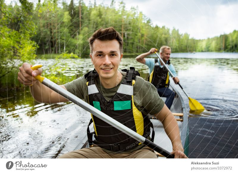 Zwei Männer in Rettungswesten beim Kanufahren auf einem Waldsee. Aktion Abenteuer offen Ausflugsziel entdecken Finnland Glück See Landschaft Lifestyle Mann