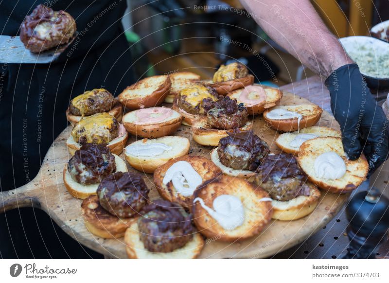 Küchenchef macht Rindfleisch-Burger im Freien auf einem Lebensmittelfestival. Fleisch Brötchen Mittagessen Teller Schreibtisch Restaurant Straße Handschuhe
