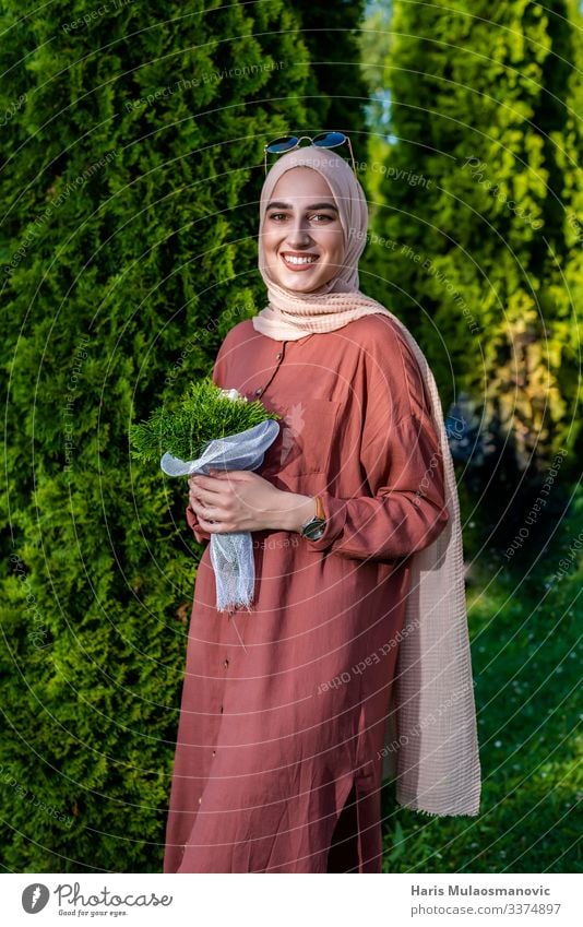 Muslimische Frau im Hidschab mit Blumenstrauß lächelt muslimisch Religion Lächeln Porträt schön beige hell heiter abschließen Bekleidung selbstbewusst Kleid