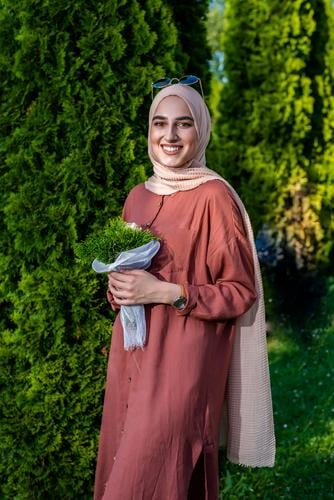 Muslimische Frau im Hidschab mit Blumenstrauß lächelt muslimisch Religion Lächeln Porträt schön beige hell heiter abschließen Bekleidung selbstbewusst Kleid