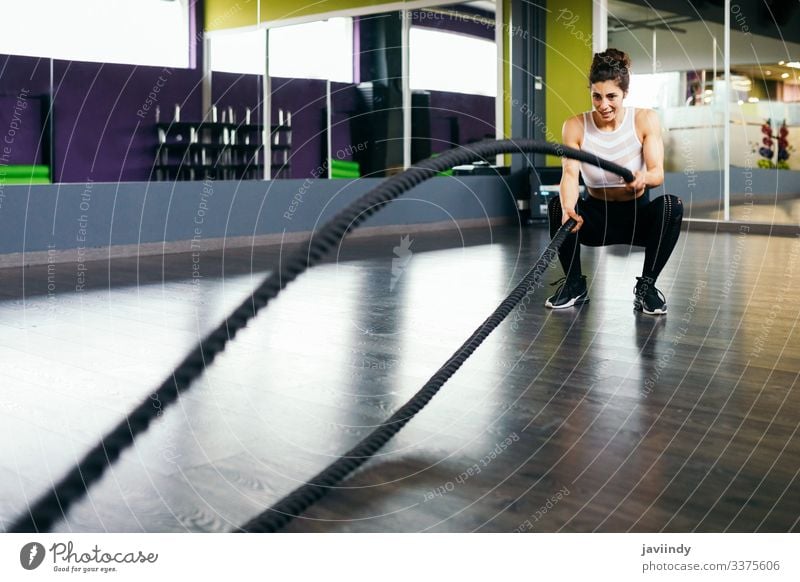 Junge und sportliche Frau, die Trainingsseile in einer Turnhalle benutzt. Seil Fitness Fitnessstudio Sportlerin Athlet aktiv jung muskulös Übung Erwachsener