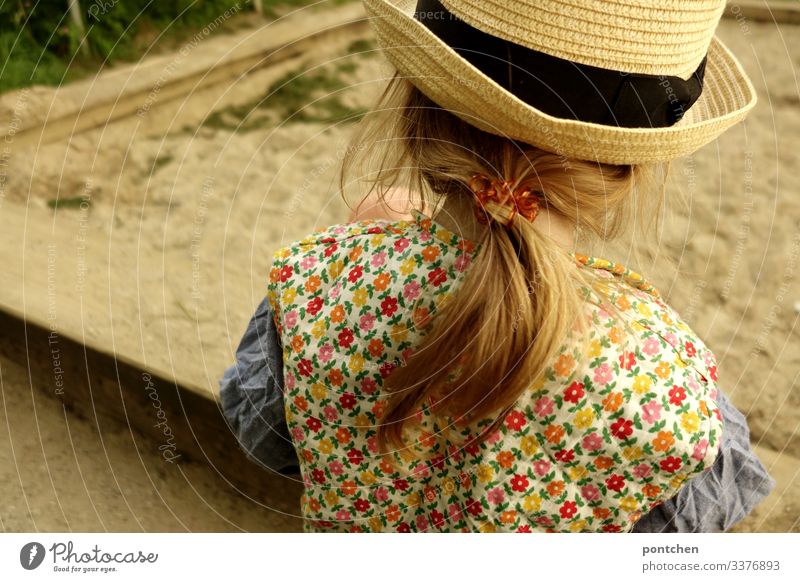 Weibliches Kleinkind von hinten spielt am Sandkasten mädchen kleinkind spielen lange haare zopf blond haargummi hipster blumenmuster kleidung weste Gras