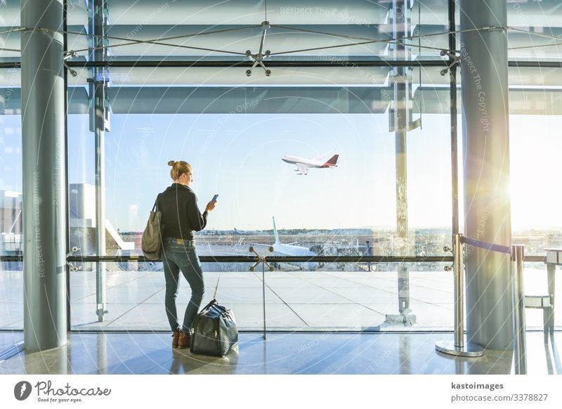 Junge lässige weibliche Reisende am Flughafen, hält Smartphone-Gerät, Blick durch die Flughafen-Gate-Fenster auf Flugzeuge auf dem Flughafen Start-und Landebahn.