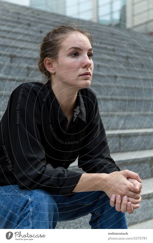 Seitenansicht Porträt einer jungen kaukasischen Frau, die auf einer Treppe im Freien sitzt Sitzen Mädchen Freitreppe Murmel Stein Wegsehen ernst stark